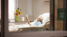 Senior in bed in hospital or nursing home reading a book.