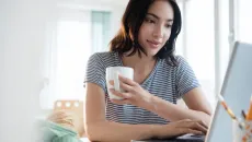 Person holding a mug and using a laptop