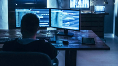 Person in dark room in front of computer monitors