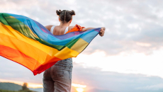 Person with rainbow flag watches sunset