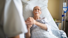 Man in hospital bed holding caregiver's hand