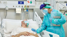 Person in PPE stands by person in hospital bed