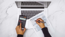 Hands at a calculator and laptop with tax form