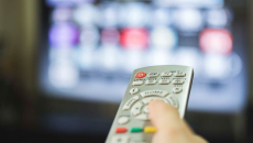 Hand operates remote with TV in background