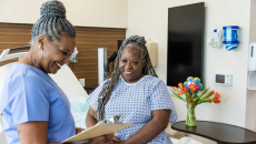 Nurse goes over information on clipboard with pleased patient sitting up in bed.