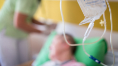 Person in hospital bed with staffer standing nearby