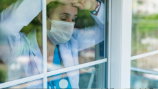 Person in PPE, exhausted, at window