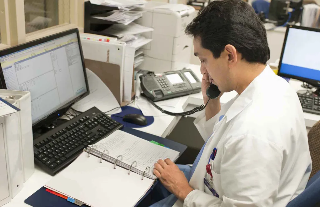 Doctor on telephone in front of book and screens Doctor on telephone in front of book and screens