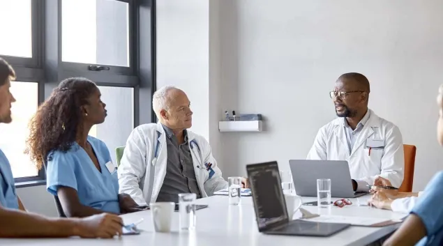Clinicians talking around a board table 