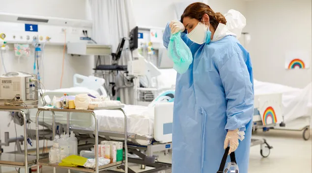 Healthcare worker wiping their forehead in PPE