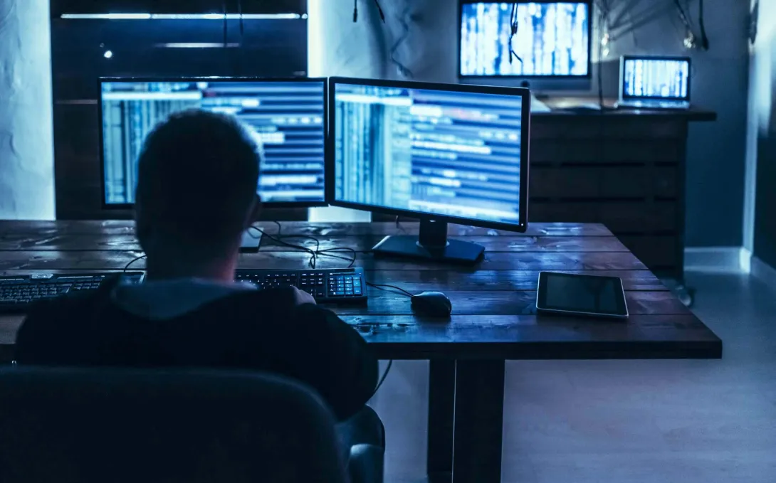 Person in dark room in front of computer monitors
