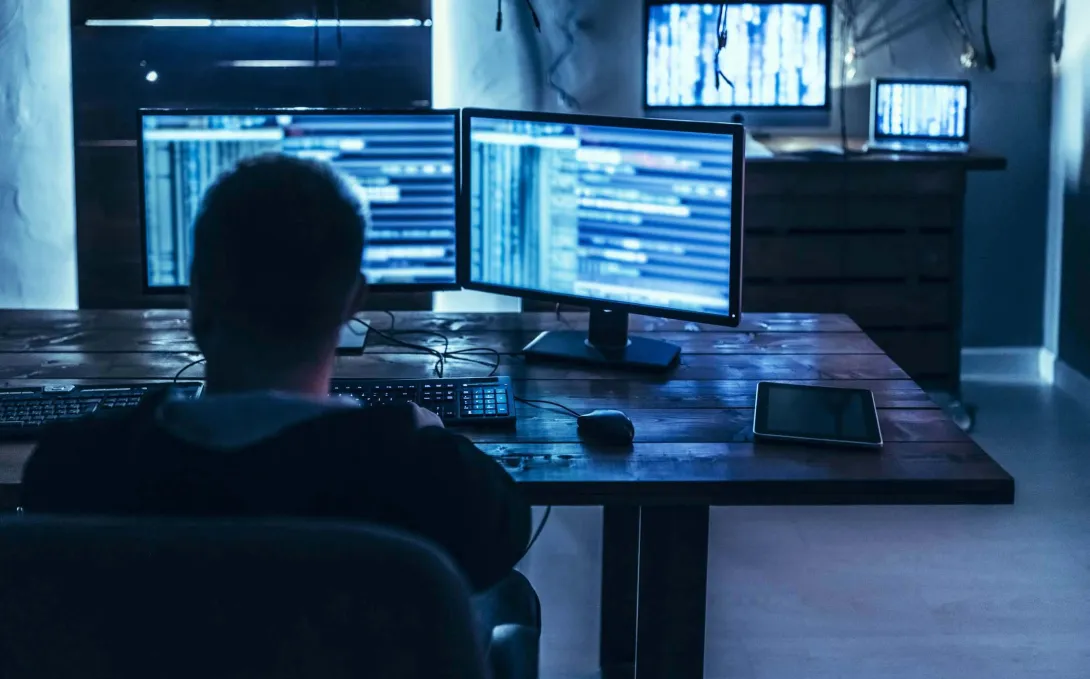 Person in dark room in front of computer monitors