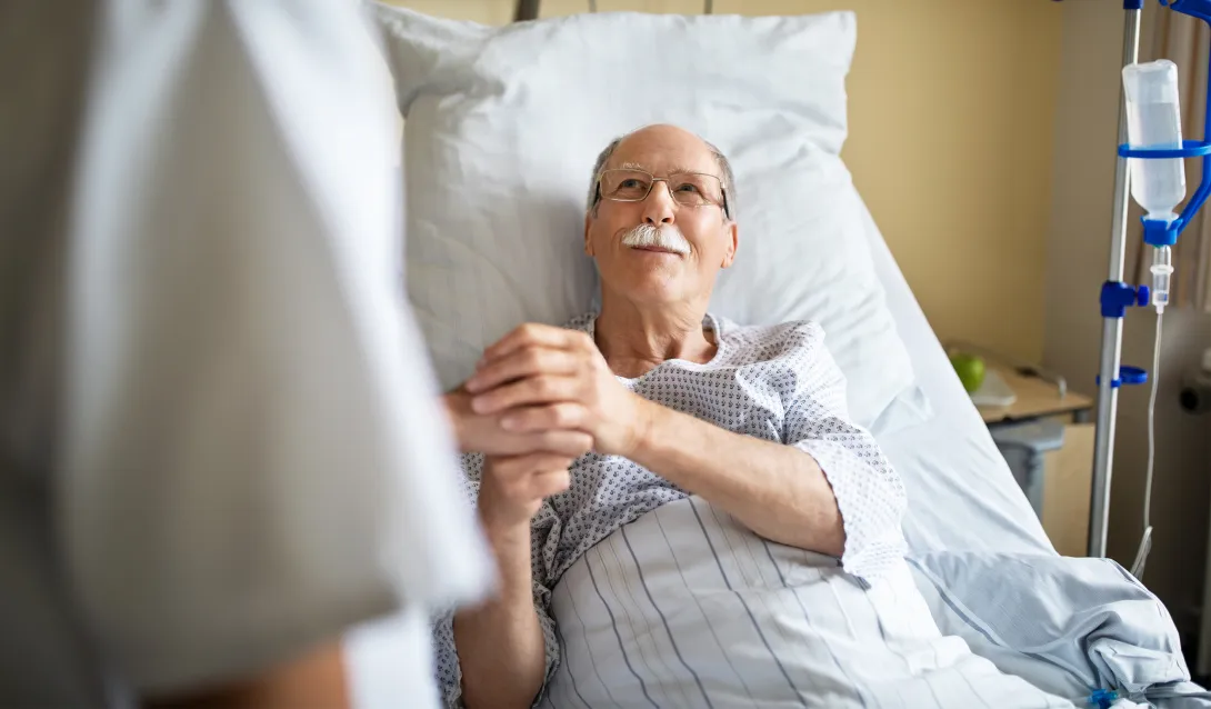 Man in hospital bed holding caregiver's hand