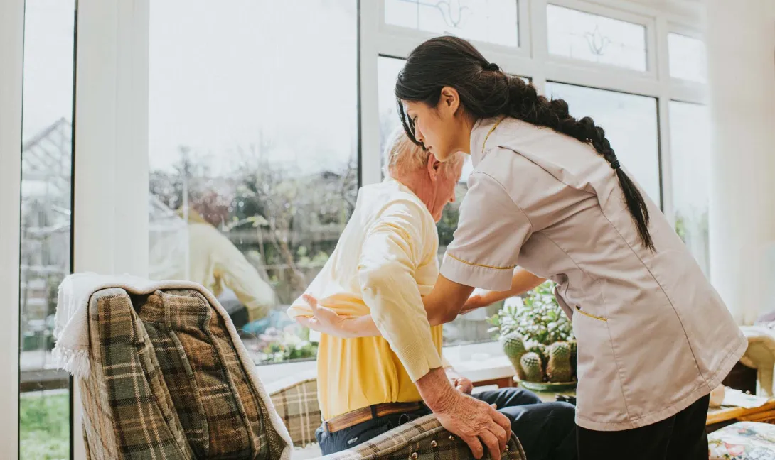 A nurse helps a resident into a chair.