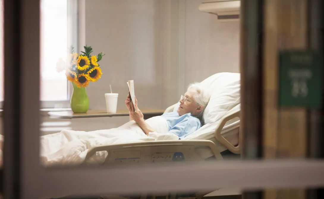Senior in bed in hospital or nursing home reading a book.