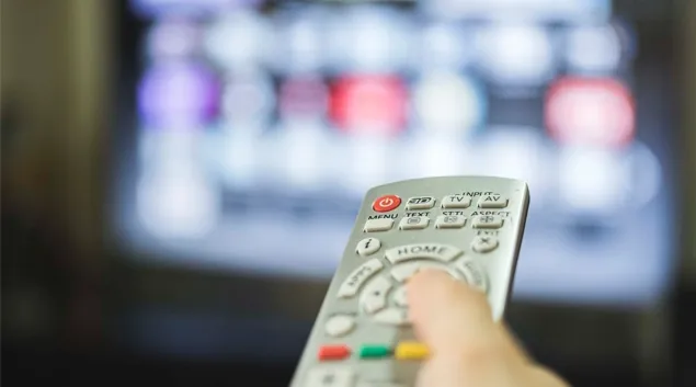 Hand operates remote with TV in background