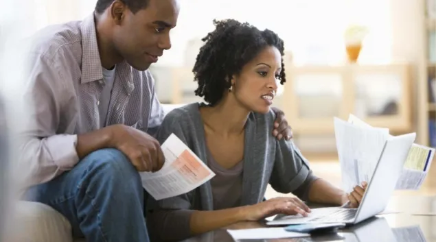 Couple on couch with bills at computer on coffee table