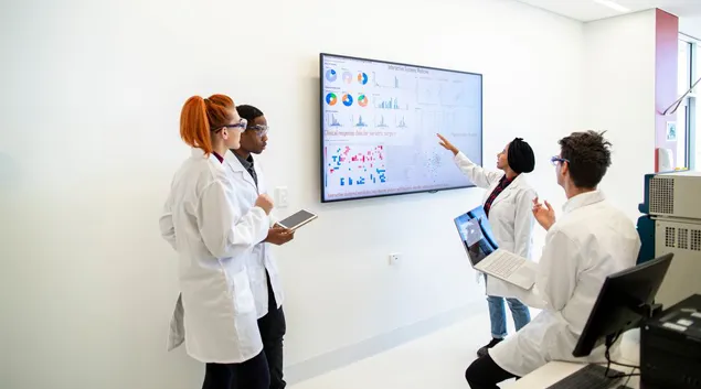 Professionals in a conference room examine a display screen with graphs