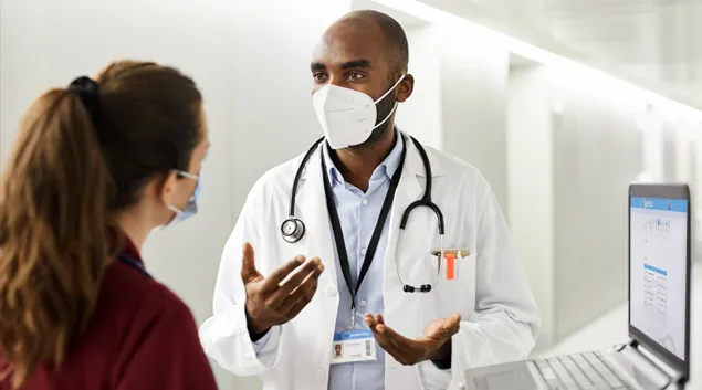 Two medical professionals speak in hospital corridor