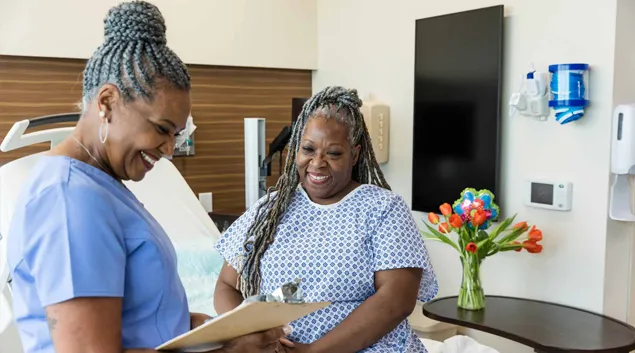 Nurse goes over information on clipboard with pleased patient sitting up in bed.
