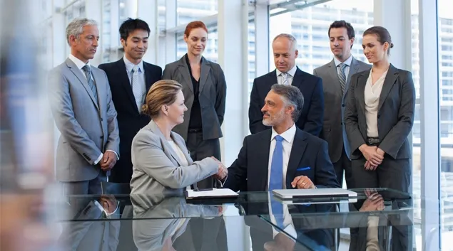 Business deal in meeting room with parties gathered around a handshake