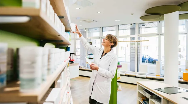 Person in lab coat at drugstore shelves