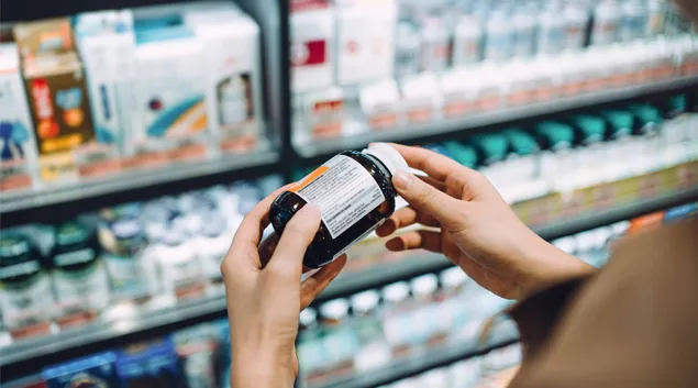 Person examines pill bottle in drug store
