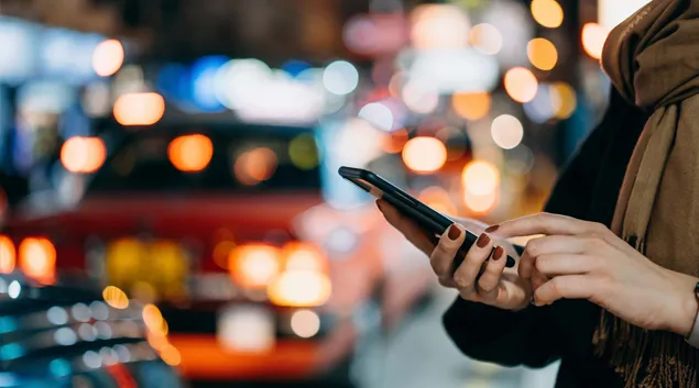 Street scene of person with phone and cars at night